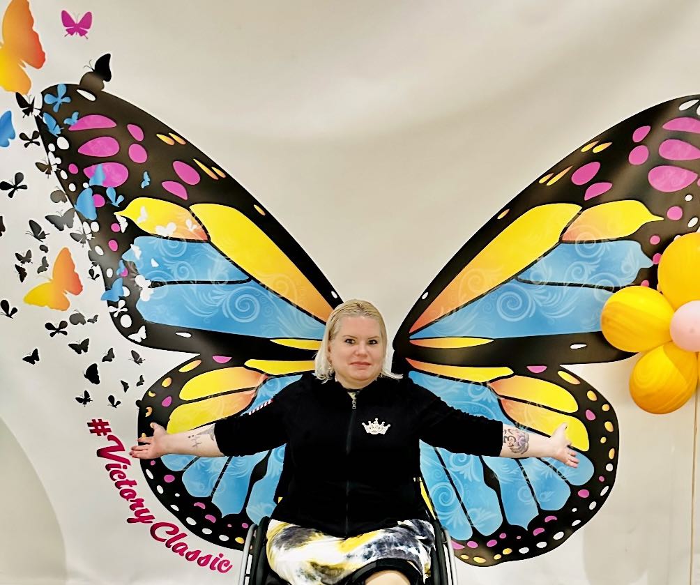 Melinda Preciado sitting in front of a butterfly wing mural with her arms spread wide